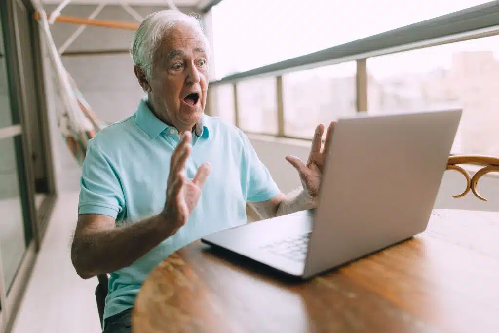 Oude man achter bureau bang voor wat hij ziet op laptop